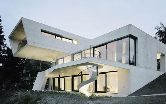 Modernes Einfamilienhaus aus Sichtbeton mit Glasgeländer, Balkon und großflächiger Verglasung.